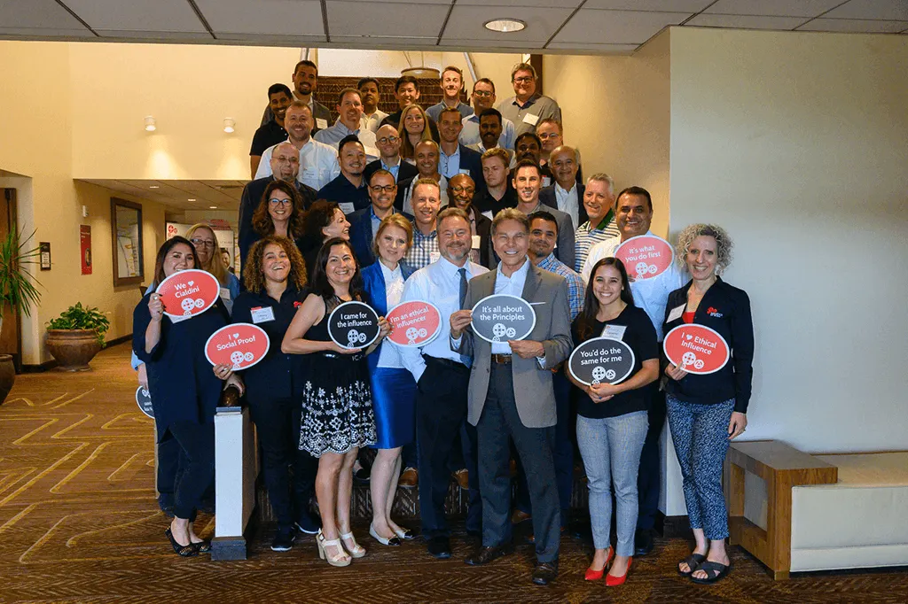 Dr. Robert Cialdini with a full workshop cohort holding signs about the principles